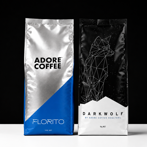 Two coffee bags from Adore Coffee Roasters standing side by side on a white surface against a black background. The left bag is silver and blue with the text 'ADORE COFFEE' and 'FLORITO'.