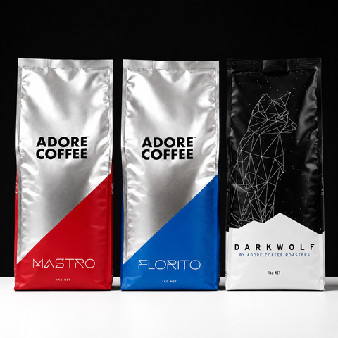 Three bags of coffee from Adore Coffee Roasters are lined up against a black background: Mastro with a red diagonal section, Florito with a blue diagonal section, and Darkwolf in a black package with a white geometric wolf logo.